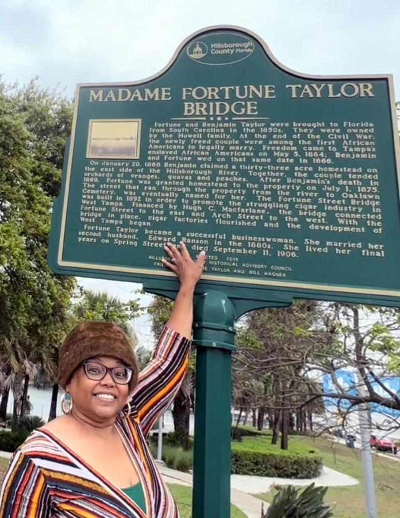 Gloria Jean Royster poses in front of a historical marker commemorating the Madame Fortune Taylor Bridge along Tampa's Riverwalk, Nov. 6, 2022, in Tampa, Fla. (Photo by Nicole Persley)