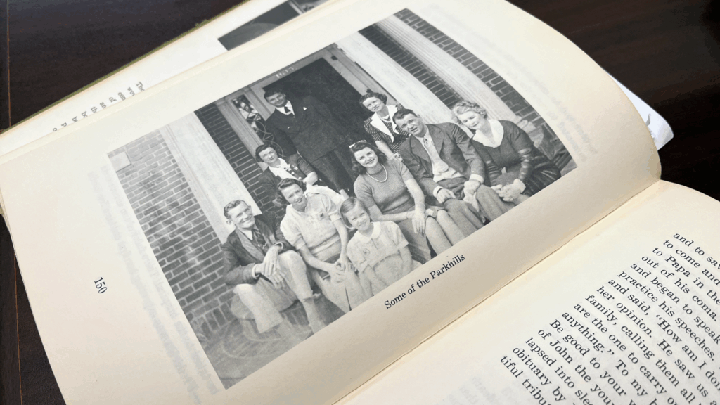 Open book on a dark table, showing a black-and-white photograph captioned “Some of the Parkhills” with a multi-generational family posed on the brick front steps of a house, page 150 visible at the bottom.