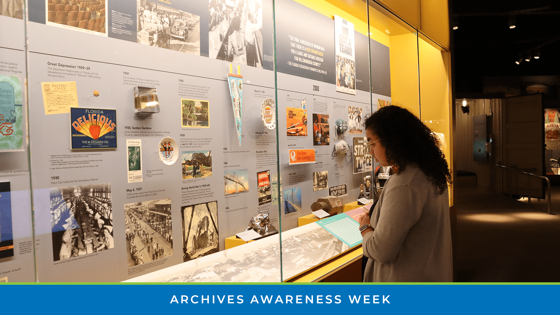 Visitor viewing artifacts and timeline displays in a museum gallery with Archives Awareness Week banner